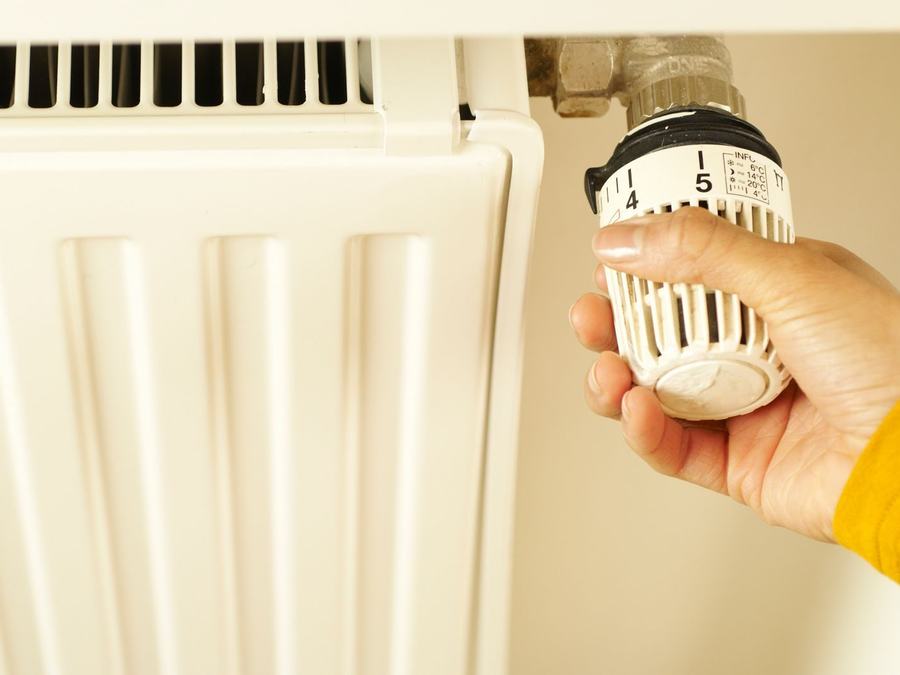 Dłoń przekręca głowicę termostatyczną kaloryfera